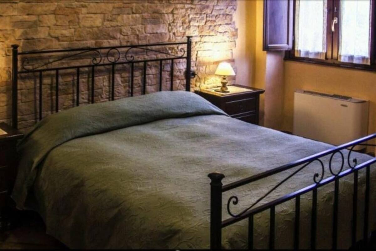 Ein Schlafzimmer mit Steinwand, einem Metallbettgestell, zwei Nachttischen mit Lampen und einem Heizkörper.