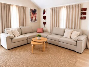 A living room with a L-shaped beige sofa, a round wooden coffee table, and a woven rug.