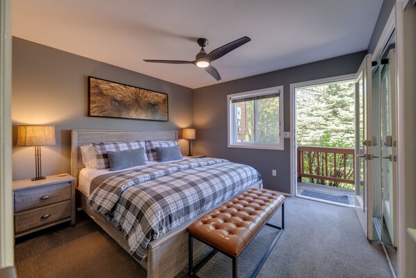 A bedroom with a bed, bedside lamps, a ceiling fan, a window, and a balcony.