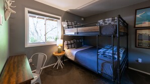 Habitación con literas, escritorio, silla, lámpara y ventana con vista a árboles.