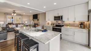 A modern kitchen with white cabinets, a marble island, and a stone fireplace. - Blue Ridge Cabin w/ Gorgeous Mountain Views! (Candler)