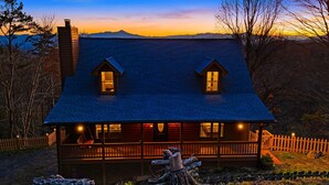 A cabin with a steeply pitched roof, two dormer windows, and a wooden deck. - Blue Ridge Cabin w/ Gorgeous Mountain Views! (Candler)
