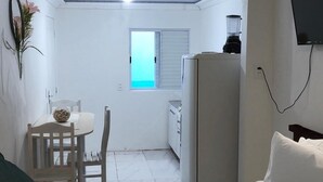A compact room with a bed, a small table with a chair, a window, a refrigerator, and a TV mounted on the wall. - Pousada Caravela (Penha)