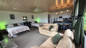 Et moderne hotelværelse med sofa, to enkelt senge, et lille tekøkken og en loftsvifte.