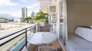 A balcony with a round table, a bed, and a view of the cityscape. - Apt in Center of Itapema 200m From the sea Ebm0122 (Itapema)
