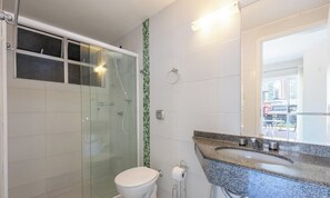 A bathroom with a glass shower enclosure, a toilet, a sink with a granite countertop, and a mirror. - Apt in Center of Itapema 200m From the sea Ebm0122 (Itapema)