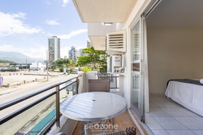 A balcony with a round table, a bed, and a view of the cityscape. - Apt in Center of Itapema 200m From the sea Ebm0122 (Itapema)