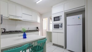 A modern kitchen with white cabinets, a built-in microwave, a refrigerator, a gas stove, and a blue vase on the counter. - Apt in Center of Itapema 200m From the sea Ebm0122 (Itapema)