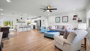 A spacious living area with a kitchen, a ceiling fan, and a dining area. - Coral Way Getaway, Walk to Beach, Near Speedway, Sleeps 8 (Port Orange)