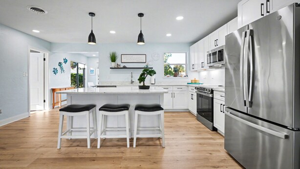 A modern kitchen with white cabinets, stainless steel appliances, and a central island with bar stools. - Coral Way Getaway, Walk to Beach, Near Speedway, Sleeps 8 (Port Orange)