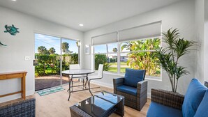 A bright room with a glass door leading to a garden, wicker furniture, and a view of greenery outside. - Coral Way Getaway, Walk to Beach, Near Speedway, Sleeps 8 (Port Orange)