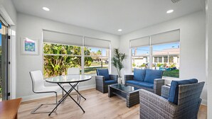 A modern living room with a glass table, wicker sofas, and a view of a garden. - Coral Way Getaway, Walk to Beach, Near Speedway, Sleeps 8 (Port Orange)