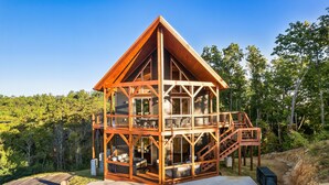 A two-story wooden cabin with a balcony, surrounded by trees. - Smoky Mountain Cabin w/ Incredible View- Perfect for Families-Indoor Heated Pool (Sevierville)