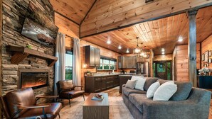 A cozy cabin interior with a stone fireplace, leather furniture, and a modern kitchen. - Smoky Mountain Cabin w/ Incredible View- Perfect for Families-Indoor Heated Pool (Sevierville)