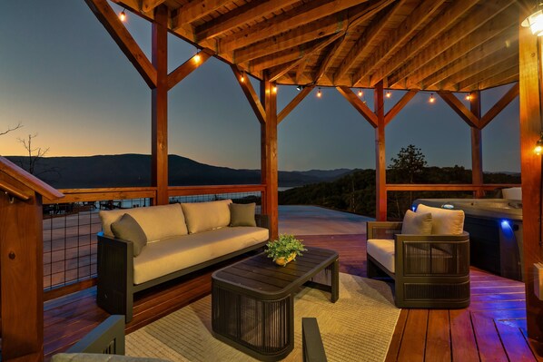 A wooden deck with a sofa, a coffee table, and a chair, overlooking a mountainous landscape. - Smoky Mountain Cabin w/ Incredible View- Perfect for Families-Indoor Heated Pool (Sevierville)