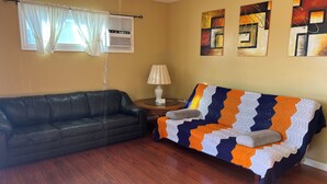 A living room with a black leather sofa, a colorful knitted throw, a wooden side table with a lamp, and a window with curtains. - The FAB House-Close to SoFi, Beaches, LAX Airport&Freeway 405&105 (Hawthorne)