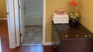 A room with a wooden floor, a dark wooden dresser with a vase of flowers, and a bathroom visible through an open door. - The FAB House-Close to SoFi, Beaches, LAX Airport&Freeway 405&105 (Hawthorne)