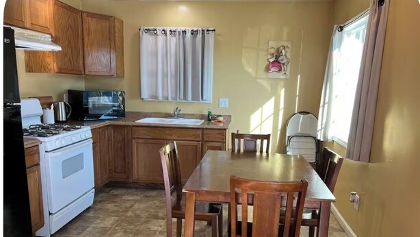 A kitchen with wooden cabinets, a stove, a microwave, and a dining table with chairs. - The FAB House-Close to SoFi, Beaches, LAX Airport&Freeway 405&105 (Hawthorne)