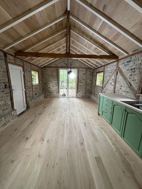 A spacious attic room with exposed wooden beams, a large window, and a green kitchen counter.