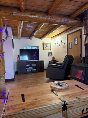 Un salon chaleureux avec un plafond en bois, une cheminée, un téléviseur et une console de jeux.