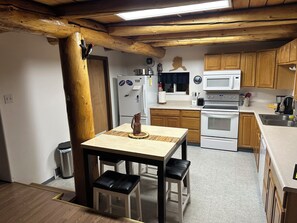 A kitchen with wooden cabinets, a white refrigerator, a microwave, an oven, and a dining table with two chairs. - Authentic Alaskan Northern Lights Lodge in the Hills of Fairbanks (Fairbanks)