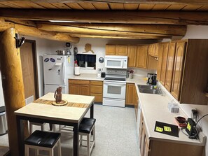 Une cuisine avec des meubles en bois, un réfrigérateur blanc, un four à micro-ondes, un four traditionnel et une table à manger avec des chaises.