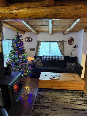 A cozy living room with a wooden ceiling, a fireplace, a Christmas tree, a sofa, and a coffee table. - Authentic Alaskan Northern Lights Lodge in the Hills of Fairbanks (Fairbanks)