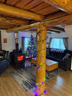 A cozy living room with a wooden ceiling, a fireplace, a Christmas tree, and a sofa. - Authentic Alaskan Northern Lights Lodge in the Hills of Fairbanks (Fairbanks)