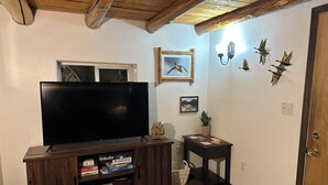 Un salon avec un meuble de rangement en bois pour l’équipement audiovisuel, un téléviseur à écran plat et une petite table sur laquelle est posée une plante.