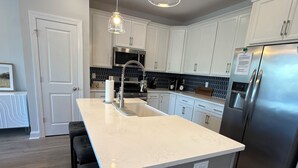 A modern kitchen with white cabinets, a stainless steel refrigerator, and a central island with bar stools.