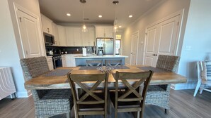 A modern kitchen with white cabinets, a central island, and a dining area with wicker chairs and a wooden table.