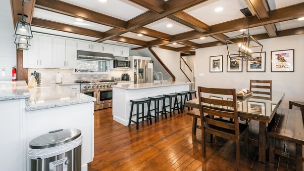 Une cuisine spacieuse avec des poutres en bois, un grand îlot central, des tabourets de bar et une table à manger avec des chaises.