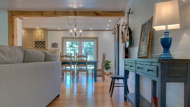 Uma sala de estar acolhedora com sofá, mesa de jantar de madeira, cadeiras e um aparador azul com abajur.