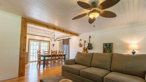 Uma sala de estar ampla com teto de madeira, ventilador de teto, um sofá, uma mesa de centro e uma área de jantar com cadeiras e mesa.