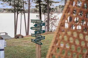 A wooden signpost with directional arrows pointing to various amenities such as a painted turtle, fire pit, lakefront, hot tub, movie theatre, playground, and game room. - The Painted Turtle: Lakefront, Hot Tub, Sauna, Theater, Game Room, Playset (Nisswa)