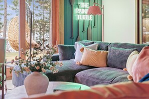 A cozy living room with a green wall, a hanging chair, and a sofa with striped cushions. - The Painted Turtle: Lakefront, Hot Tub, Sauna, Theater, Game Room, Playset (Nisswa)
