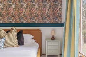 A bedroom with a floral-patterned ceiling, a bed with striped and solid pillows, a bedside table with a lamp, and a window with curtains. - The Painted Turtle: Lakefront, Hot Tub, Sauna, Theater, Game Room, Playset (Nisswa)