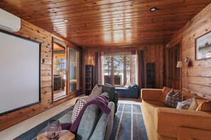 A cozy cabin interior with a wooden ceiling, a large window with curtains, a sofa, and a television. - The Painted Turtle: Lakefront, Hot Tub, Sauna, Theater, Game Room, Playset (Nisswa)