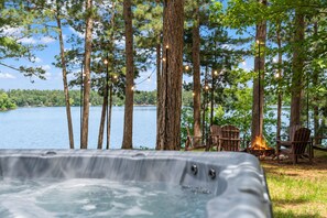 A hot tub with a view of a lake and trees, surrounded by Adirondack chairs. - The Painted Turtle: Lakefront, Hot Tub, Sauna, Theater, Game Room, Playset (Nisswa)