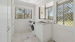 A compact laundry room with a washing machine, a sink, and a window providing natural light. - Moonee Stayz – House - Where Moonee estuary meets the ocean (Moonee Beach)