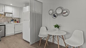 A modern kitchen with white cabinets, a microwave, and a refrigerator. There is a dining area with a round table and two white chairs.