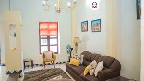 A living room with a brown sofa, a yellow armchair, a small table, a lamp, and a window with a red curtain. - Casa con Encanto Centro Mazatlan 4 Rec (Mazatlán)
