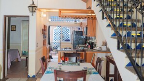 A dining area with a table set for four, a staircase with a black railing, and a kitchen in the background. - Casa con Encanto Centro Mazatlan 4 Rec (Mazatlán)