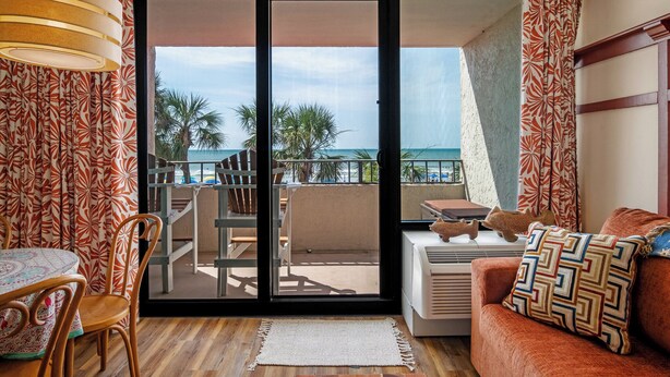 A room with a balcony, a table with chairs, and a sofa with a patterned pillow. - Oceans 211 is a colorful newly renovated suite in the popular Oceans Reef resort (Myrtle Beach)