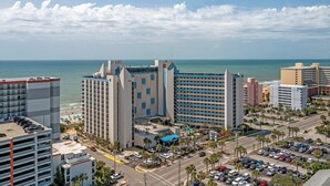 A coastal hotel with multiple high-rise buildings, a parking lot, and a beach area with umbrellas. - Oceans 211 is a colorful newly renovated suite in the popular Oceans Reef resort (Myrtle Beach)