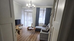 A spacious living area with a wooden floor, a sofa, a small table, and a TV. - Gdynia City Center 2 by Grand Apartments (Gdynia)