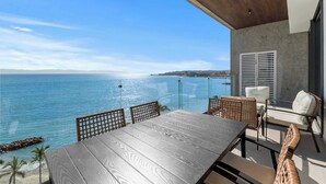 Een houten tafel en rieten stoelen op een balkon met uitzicht op een heldere blauwe zee.