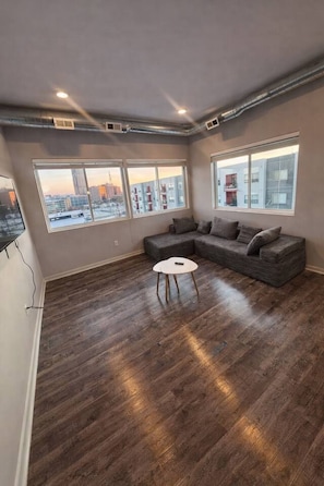 A modern living room with a sectional sofa, a round coffee table, and large windows offering city views.