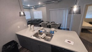 A compact kitchen with a sink, a dining area with a table and chairs, and a sofa in the background.