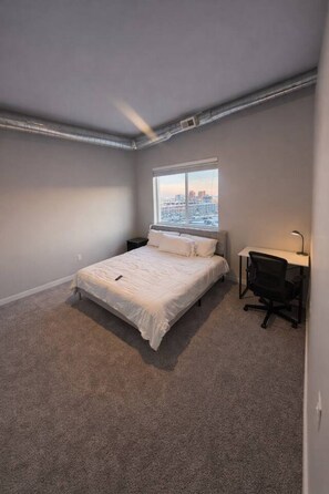 A bedroom with a bed, a desk, and a window with a city view.